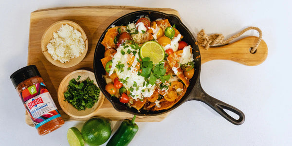 Cast iron skillet holds sizzling sheet pan nachos topped with fresh cilantro, cotija cheese, and lime slices.  
