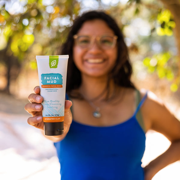Woman holds out tube of hydrating clay facial mud for clear skin. 
