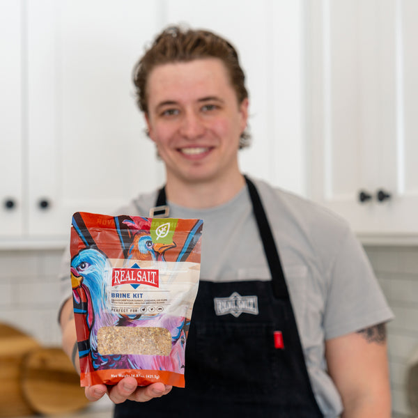 Man smiles while holding a bag of Real Salt Brine Kit in a home kitchen. 
