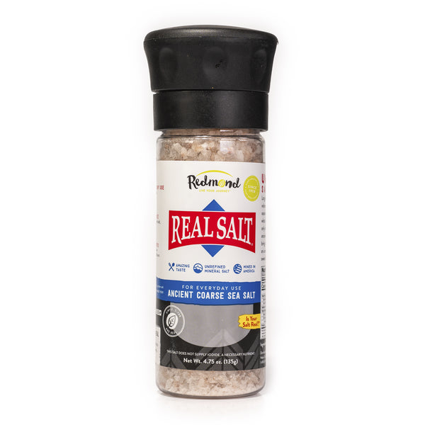 A clear grinder displays Redmond Real Salt Ancient Coarse Sea Salt. The grinder features a black top for easy dispensing. 

